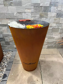 Cylindrical metal grill with food on a stone patio